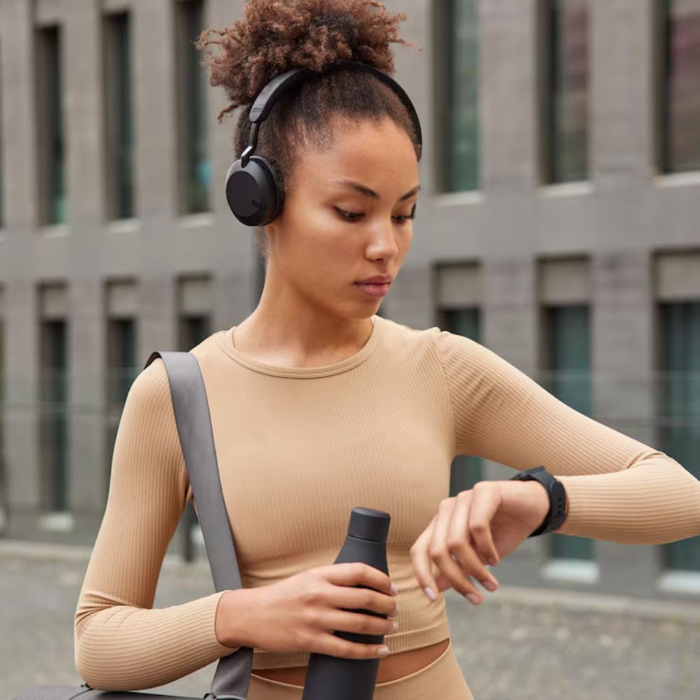Woman wearing headphones and checking her smartwatch outdoors.